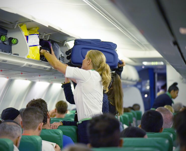 a flight attendant struggles to help a passenger stow their luggage in the overhead bin