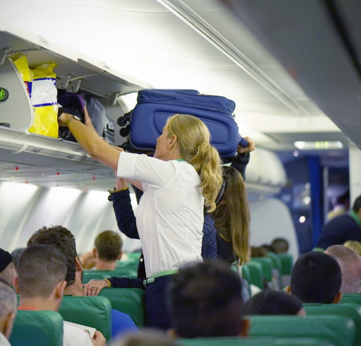 a flight attendant struggles to help a passenger stow their luggage in the overhead bin