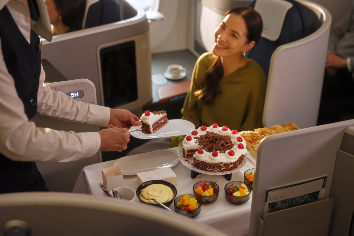 a lufthansa crew members serving a business class passenger a slice of cake